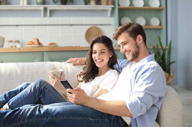 Jeune couple regardant du contenu en ligne sur un smartphone assis sur un canapé à la maison dans le salon.