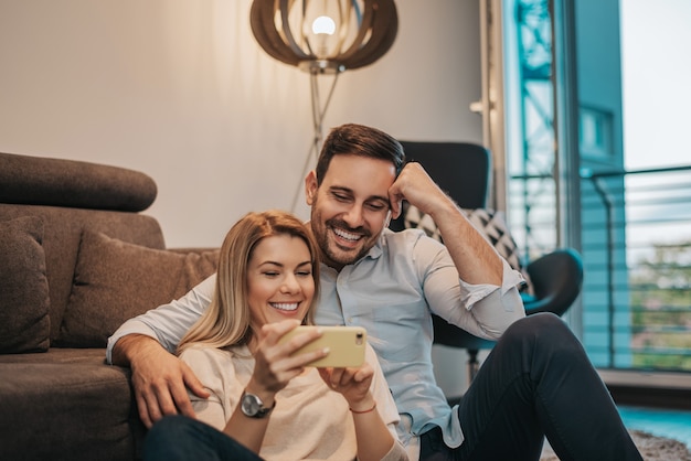 Jeune couple en regardant l&#39;écran d&#39;un téléphone portable ensemble dans leur maison.