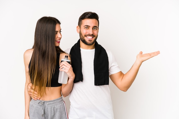 Jeune couple de remise en forme caucasien isolé montrant un espace de copie sur une paume et tenant une autre main sur la taille.