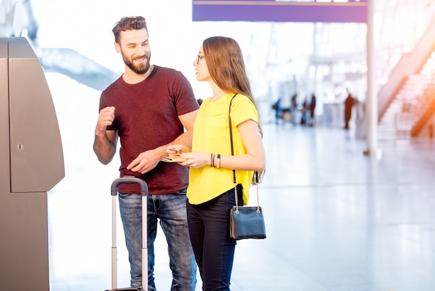 Jeune couple retirant de l'argent à l'aide d'un guichet automatique à l'aéroport pendant leur voyage