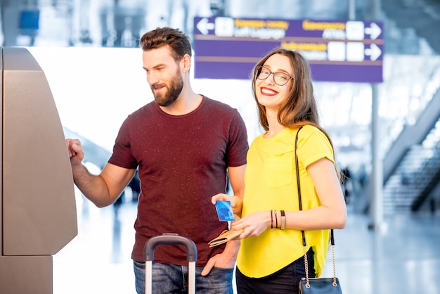 Jeune couple retirant de l'argent à l'aide d'un guichet automatique à l'aéroport pendant leur voyage