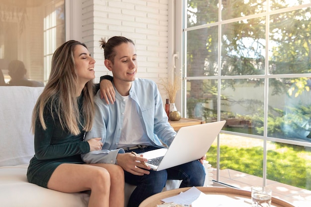 Jeune couple riant souriant et détendu utilisant et regardant un ordinateur portable sur internet dans le salon