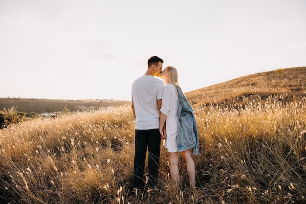 Jeune couple romantique dans un champ ouvert, main dans la main et s'embrasser.