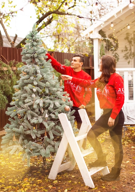 Photo jeune couple romantique décore l'arbre de noël à l'extérieur avant noël. profiter de passer du temps ensemble au réveillon du nouvel an.