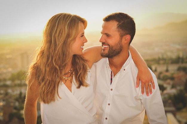 Un jeune couple romantique heureux contre la ville au coucher du soleil.