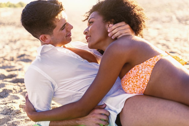 Jeune couple romantique multiculturel étreignant allongé sur la plage.