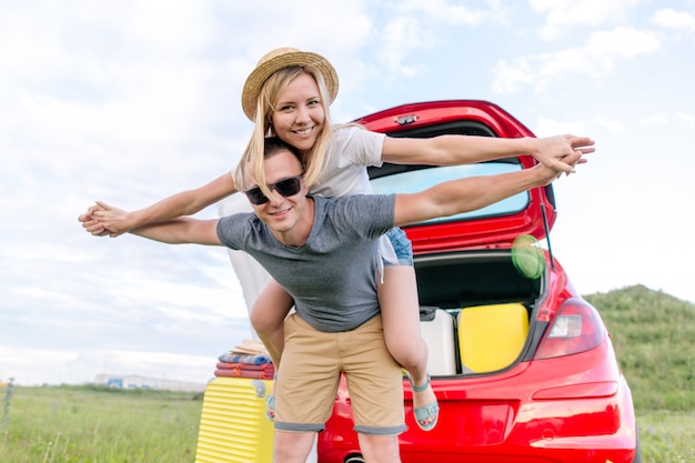 Jeune couple s'amusant à l'extérieur en se chevauchant devant la voiture avec des choses pour le camping