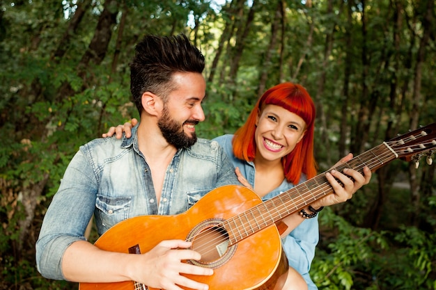 Jeune couple s&#39;amusant avec la guitare dans le parc.
