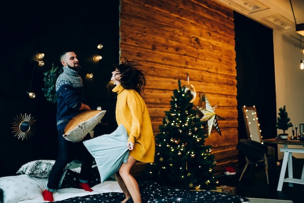 Jeune couple s'amusant avec des oreillers se battre sur le lit à Noël