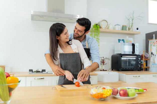 Jeune couple s'amusant tout en préparant le petit-déjeuner ensemble dans une belle matinée cuisiner ensemble relation de cuisine trancher les tomates ensemble pour les utiliser dans les salades