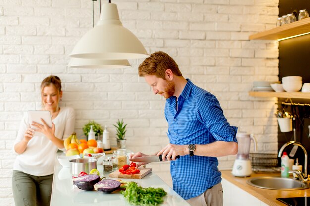 Jeune couple s&#39;amuse dans une cuisine moderne en intérieur tout en préparant des plats de légumes pour le déjeuner