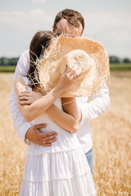 Jeune couple s'embrassant se cachant derrière un chapeau dans le domaine