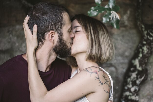 Jeune couple s'embrassant sous un arbre escaladant un mur