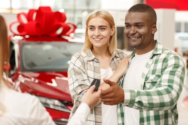 Photo jeune couple s'embrassant tout en recevant les clés de leur nouvelle voiture d'un vendeur de voitures.