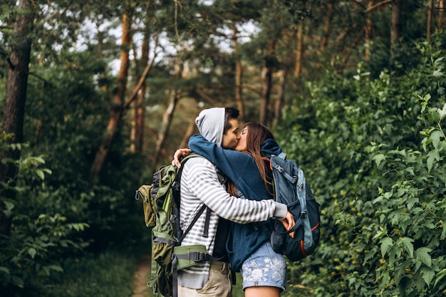 Jeune couple avec sacs à dos sur le dos dans la forêt. Un homme aimant embrasse sa belle petite amie lors d'une randonnée dans les bois