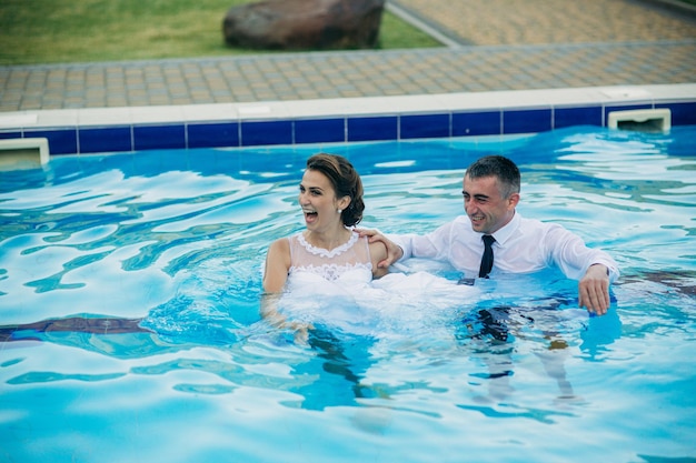 Jeune couple sautant dans la piscine en costume de mariage et robe de mariée le jour de leur mariage