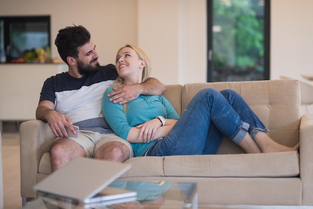 Un jeune couple se détend sur le canapé du salon de luxe, à l'aide d'un ordinateur portable et d'une télécommande