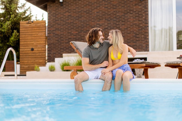 Jeune couple se détendre au bord de la piscine dans la cour de la maison