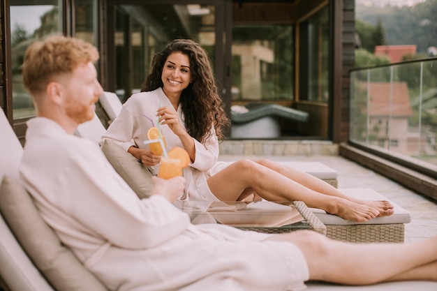 Jeune couple se détendre sur des lits et boire du jus d'orange frais sur la terrasse extérieure