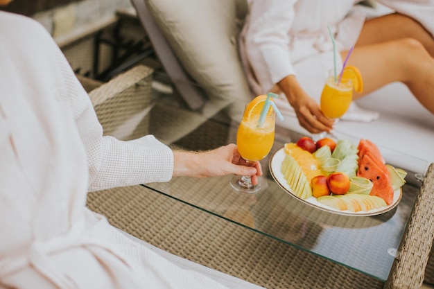 Jeune couple se détendre sur des lits et boire du jus d'orange frais sur la terrasse extérieure