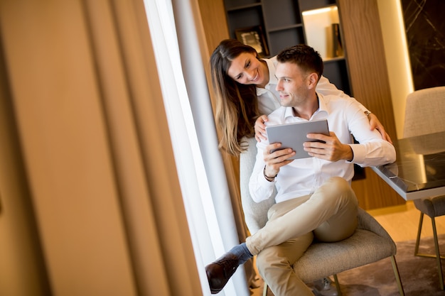 Jeune couple se détendre à la maison à l'aide de tablette numérique dans le salon par la fenêtre