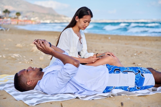 Jeune couple se détendre sur la plage allongé assis sur le sable avec des smartphones