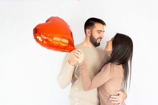 Jeune couple se regardant et se serrant dans ses bras tout en tenant un ballon en forme de coeur rouge