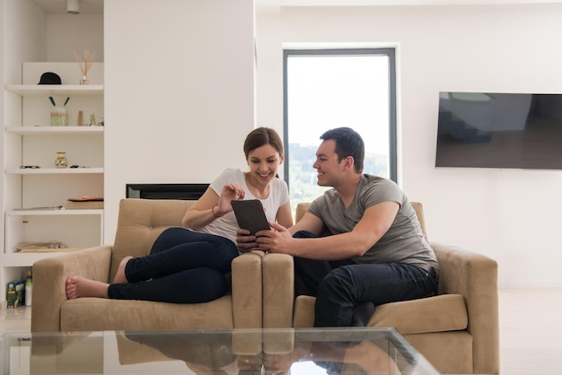 Jeune couple se relaxant dans une maison luxueuse avec des tablettes lisant dans le salon sur le canapé-lit.