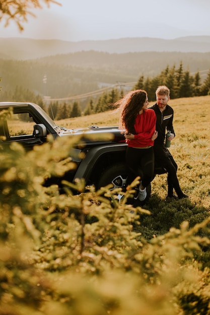 Jeune couple se reposant près d'un capot de véhicule tout-terrain à la campagne