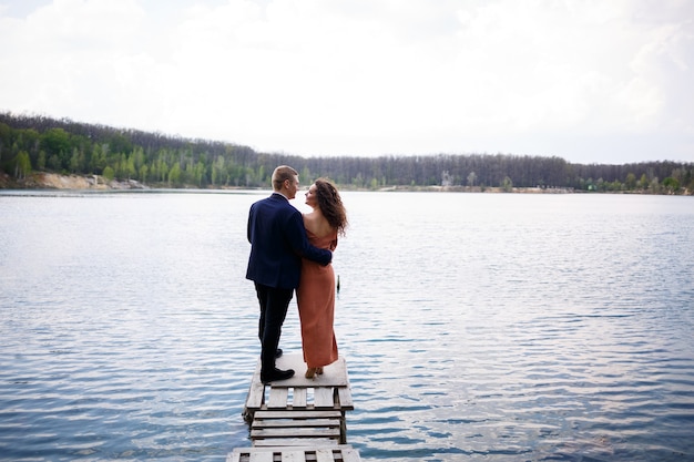 Un jeune couple se tenant la main sur un pont en bois au milieu d'un lac bleu. Maçonnerie sur l'île sur fond d'arbres. Nature, paysage. Romance et amour, couple heureux