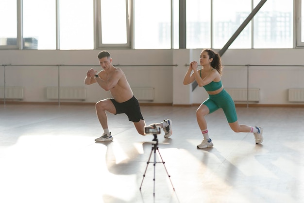 Jeune couple séduisant garçon et fille faisant de l'exercice dans la salle de sport enregistrant des blogs vidéo sur le sport