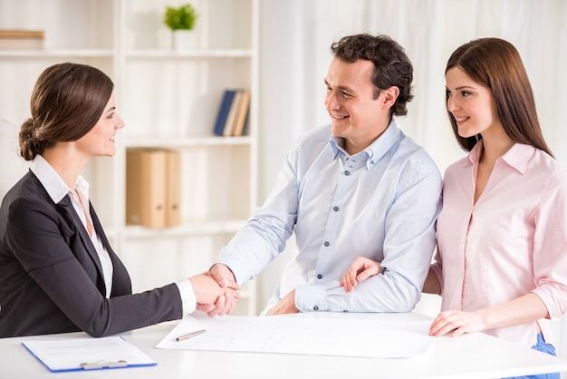 Jeune couple signant un contrat financier avec un agent immobilier féminin.