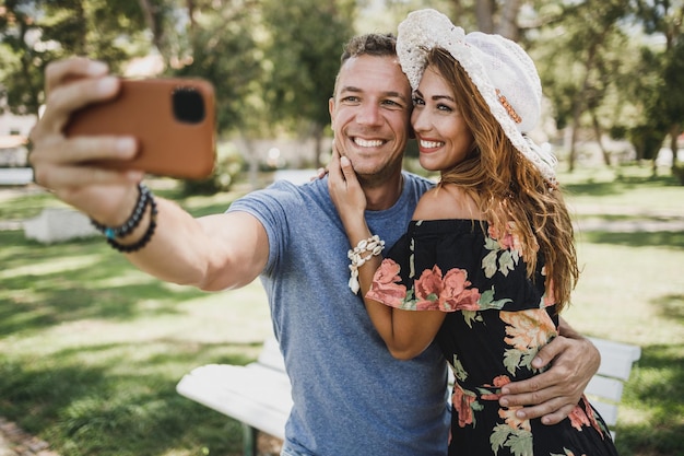 Jeune couple souriant faisant un selfie avec leur smartphone tout en profitant d'une journée d'été dans le parc.