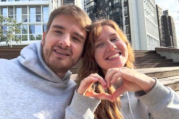 Jeune couple souriant regardant l'écran du téléphone portable tout en prenant un selfie contre la ville