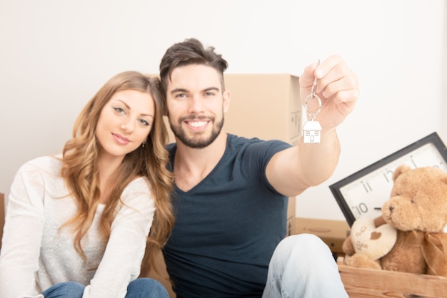 Jeune couple souriant tenant leurs nouvelles clés de maison, concept immobilier et de relocalisation