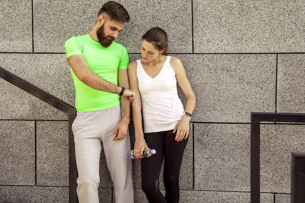 Un jeune couple sportif se repose et vérifie sa montre de fitness ensemble, boit de l'eau. concepts sportifs et technologiques.