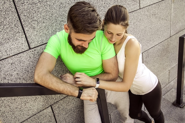 Un jeune couple sportif se repose et vérifie sa montre de fitness ensemble. concepts sportifs et technologiques.