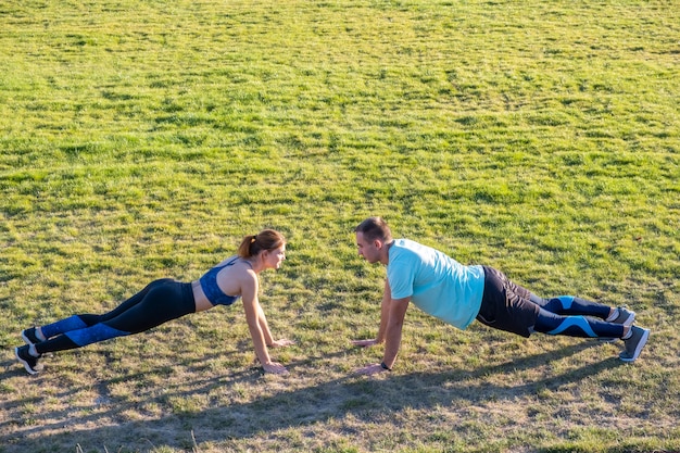 Jeune couple de sportifs en forme garçon et fille, faire de l'exercice sur l'herbe verte du stade public à l'extérieur.