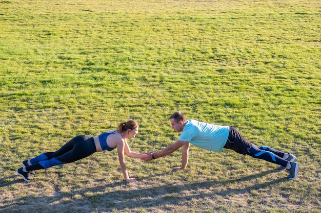 Jeune couple de sportifs en forme garçon et fille, faire de l'exercice sur l'herbe verte du stade public à l'extérieur.