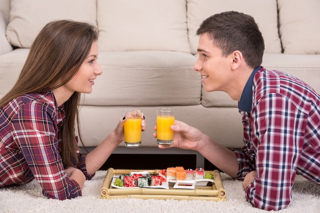 Jeune couple avec sushi et boissons sur le sol à la maison.