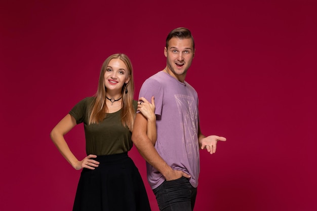 Jeune couple sympa qui pose en studio, exprime des émotions et des gestes, souriant, sur fond bordeaux