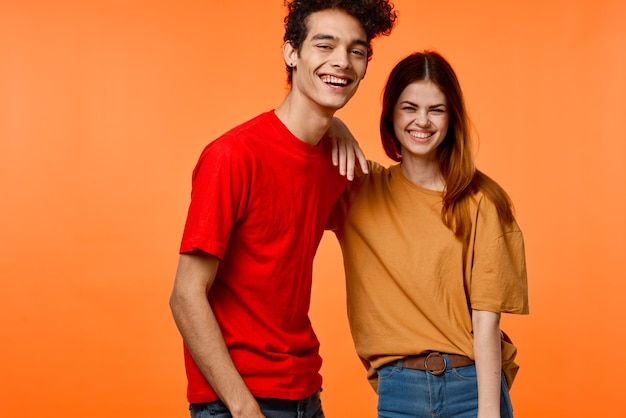 Un jeune couple en t-shirts multicolores de joie coupé vue arrière-plan orange photo de haute qualité