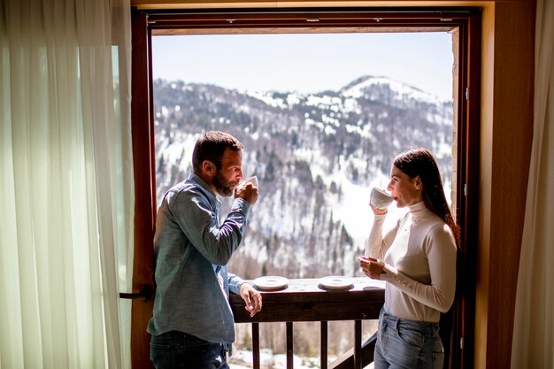 Jeune couple avec des tasses de thé chaud à la fenêtre d'hiver