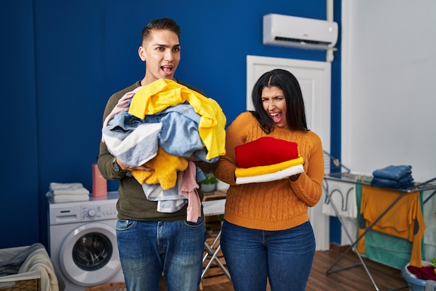 Jeune couple tenant du linge sale et propre célébrant fou et étonné du succès avec les yeux ouverts hurlant d'excitation.