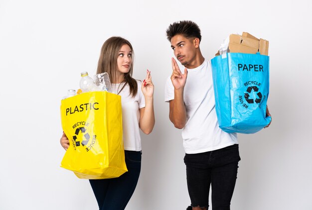 Jeune couple tenant un sac plein de plastique et de papier sur blanc avec les doigts qui se croisent et souhaitant le meilleur