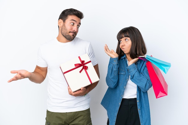 Jeune couple tenant des sacs à provisions et présent isolé sur fond blanc faisant un geste sans importance tout en soulevant les épaules