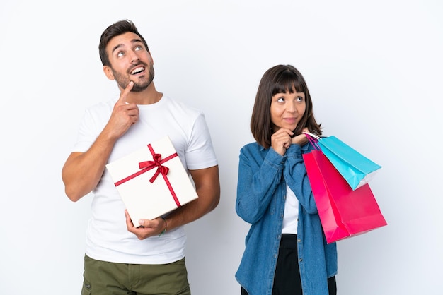 Jeune couple tenant des sacs à provisions et présent isolé sur fond blanc en pensant à une idée tout en levant les yeux