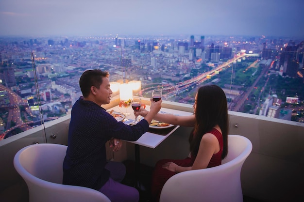 Un jeune couple tintant des verres à vin lors d'un dîner romantique sur le toit la nuit.
