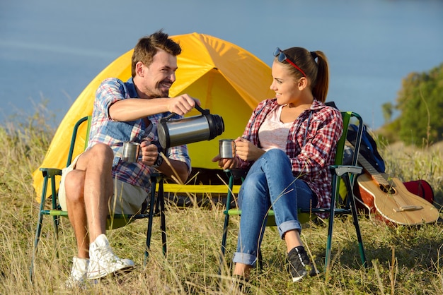 Jeune couple de touristes buvant du thé près du camp de tentes.