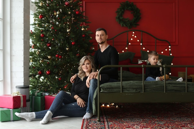 Jeune couple traditionnel avec petit fils mignon posant près de l'arbre de Noël dans le décor pour le nouvel an...